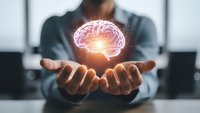 Businessman holding glowing brain hologram in cupped hands representing artificial intelligence, innovation and mental health concepts in modern office.
