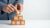 Businessman stacking wooden blocks with insurance icons including health, car, travel, family and home, symbolizing comprehensive coverage planning.
