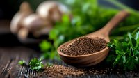 Ground black pepper in wooden spoon with fresh parsley and mushrooms on rustic dark wooden table, macro food photography with soft focus.