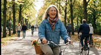 Happy mature woman cycling through autumn park with basket, enjoying outdoor recreation and healthy lifestyle in golden fall foliage.