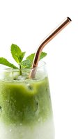 Refreshing iced green matcha mojito with fresh mint leaves and a copper metal straw in a dewy glass on white background.