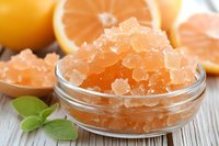 Orange citrus bath salts in glass bowl with fresh grapefruit slices and mint leaves for spa relaxation and aromatherapy wellness treatment.