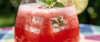 Refreshing watermelon cocktail with ice cubes, mint leaves, and lemon slice in a glass on a colorful surface outdoors.