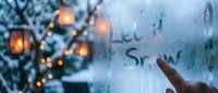 Finger writing Let it Snow on a foggy winter window with glowing lanterns and snowy trees in the background, cozy holiday atmosphere.