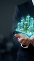 Businessman in dark suit holding glowing holographic sustainable city with green buildings and wind turbines, representing eco-friendly urban development and smart technology innovation.