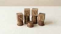 Wooden letter blocks spelling SAVE positioned on stacks of copper coins representing financial savings and money management concepts for budgeting education.