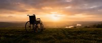 Empty wheelchair in rural field at golden hour sunset, symbolizing hope, recovery, and overcoming challenges in healthcare and rehabilitation contexts.