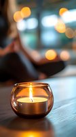 Glowing tealight candle in round glass holder on wooden surface with soft bokeh lights in background creates peaceful atmospheric mood for relaxation.