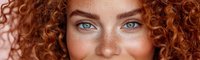 Close up portrait of young woman with bright blue eyes and natural red curly hair, freckles on face against neutral background. Fresh natural beauty concept.