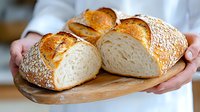 Fresh homemade crusty bread loaves with golden brown crust and soft white crumb texture, served on wooden cutting board, held by baker in white apron.