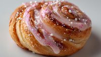 Glazed cinnamon roll pastry with pink icing and pearl sprinkles on white background. Sweet bakery dessert for breakfast menu and cafe advertising.