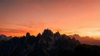 Dramatic mountain peaks silhouetted against vibrant orange and pink sunset sky creating stunning alpine landscape for outdoor adventure and nature photography.