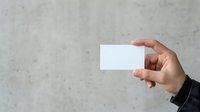 Person with medium skin tone holding blank white business card against concrete wall background for branding mockup and corporate identity presentation.