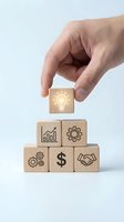 Hand placing wooden cube with lightbulb icon on pyramid of business blocks featuring growth chart, gears, dollar sign and handshake symbols on white background.