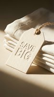 Folded white linen fabric with a textured paper price tag reading Save Big, tied with twine, in warm natural light for sale and retail concepts.