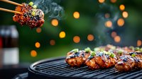 Grilled chicken wings with sesame seeds and green onions on barbecue grill with steam rising and bokeh lights in background, close up food photography.