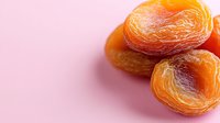 Sweet dried apricots on pink background, close up view of healthy natural snack. Organic dried fruit with wrinkled texture and vibrant orange color.