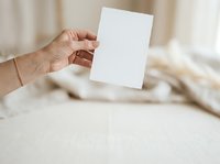 Hand holding blank white card mockup for branding, greeting, or business presentation design on neutral beige fabric background.