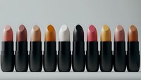 Row of matte lipsticks in nude and earth tone shades arranged in black tubes on light background, minimal makeup product photography for beauty and cosmetics marketing.