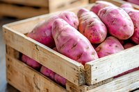 Fresh pink sweet potatoes in rustic wooden crate, close up view of organic farm produce with natural lighting and selective focus for food photography.