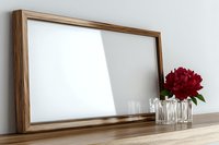 Empty wooden picture frame mockup on shelf with glass vase and red peony flower against white wall, modern minimal home decor styling.