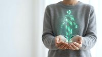 Businesswoman holding glowing green holographic human figure in cupped hands representing digital healthcare technology and medical innovation concepts.