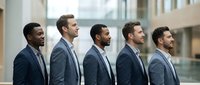 Five diverse professional businessmen in suits standing in profile view inside modern corporate office building with natural lighting for teamwork concepts.