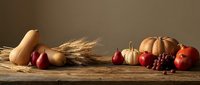 Autumn harvest display with pumpkins, gourds, apples, grapes and wheat stalks arranged on rustic wooden table for seasonal decoration and thanksgiving concepts.