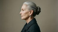 Senior woman with gray hair styled in a bun, wearing dark clothing, shown in profile against neutral background for portrait and aging concepts.