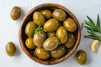 Fresh green olives in wooden bowl with rosemary and garlic on white background, top view. Mediterranean cuisine ingredients for healthy eating.