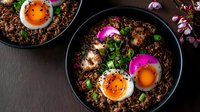 Asian rice bowl with soft-boiled eggs, pickled red onions, and fresh herbs served in dark ceramic bowls. Vibrant purple and orange colors create appetizing contrast.