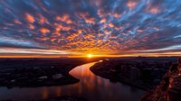 Dramatic sunset over winding river with vibrant orange and purple clouds reflecting in calm water, aerial landscape view for nature and travel content.