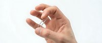 Close-up of a hand holding a small transparent capsule or pill against a white background, suitable for pharmaceutical, healthcare, and medical supplement advertising.