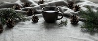 Cozy winter scene with steaming coffee cup surrounded by pine cones and evergreen branches on soft blanket for holiday seasonal comfort and warmth concepts.