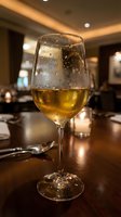 Glass of white wine with condensation droplets on elegant restaurant table with warm ambient lighting and blurred dining room background.
