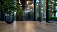 Modern office interior with green plant in dark blue pot on wooden table surface, blurred glass walls and bokeh lights background. Suitable for business concepts.