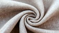 Natural beige linen fabric with twisted spiral fold showing textile texture and weave pattern for home decor and fashion design projects.