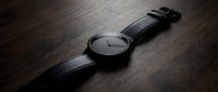 Minimalist black watch with leather strap on wooden surface, suitable for luxury product photography, fashion editorials, and lifestyle branding projects.
