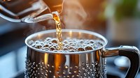 Hot coffee being poured into metallic mug with steam rising and morning sunlight creating golden glow, close up view showing rich coffee bubbles and aromatic brew.