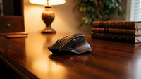 Wireless computer mouse on wooden desk with warm lamp lighting and books in background, suitable for office and technology concepts.