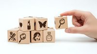 Hand placing wooden cube with magnifying glass icon onto stack of blocks featuring beauty and cosmetics symbols on white background.