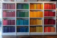 White bookshelf with books arranged in rainbow color spectrum from pink to red, creating vibrant organized display for library, bookstore, or home decor.