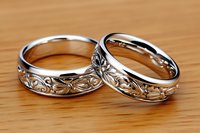 Elegant silver wedding bands with intricate floral and vine pattern engraving on wooden surface, symbolizing eternal love and commitment in marriage ceremony.