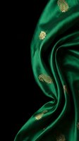 Luxurious emerald green silk fabric with golden paisley embroidery flowing in elegant waves against black background for premium textile design projects.