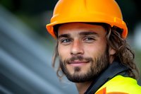 Confident construction worker wearing orange hard hat and safety vest smiles at camera, showcasing professional workplace safety and positive attitude.