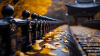Black metal fence with fallen autumn leaves on rainy day, traditional Asian architecture in background creates moody atmospheric scene with golden foliage and bokeh effect.
