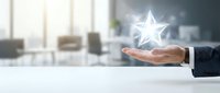 Businessman hand holding glowing star icon above desk in modern office environment, representing success, achievement, excellence, and business growth concept.