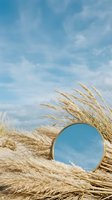 Round mirror nestled in golden pampas grass against blue sky with white clouds. Natural boho decor concept for interior design and wellness branding.