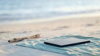 Smartphone lying on wet sand at shoreline with ocean waves and beach in soft focus background.