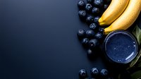 Fresh blueberry smoothie in glass with ripe bananas and scattered berries on dark background, healthy breakfast concept with copy space.